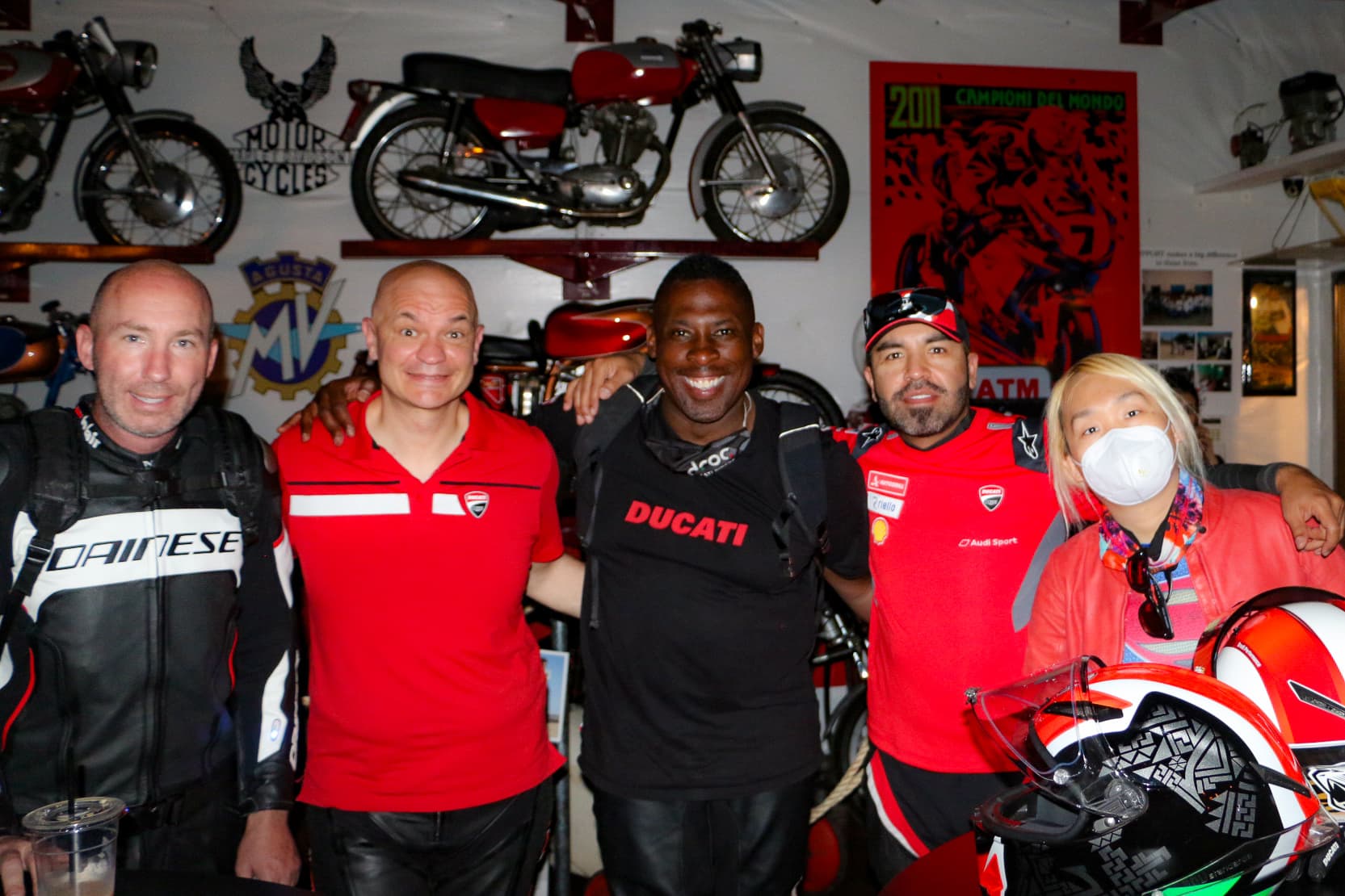 Ducati riders in red gear smiling together at a club event surrounded by vintage bikes in Orange County