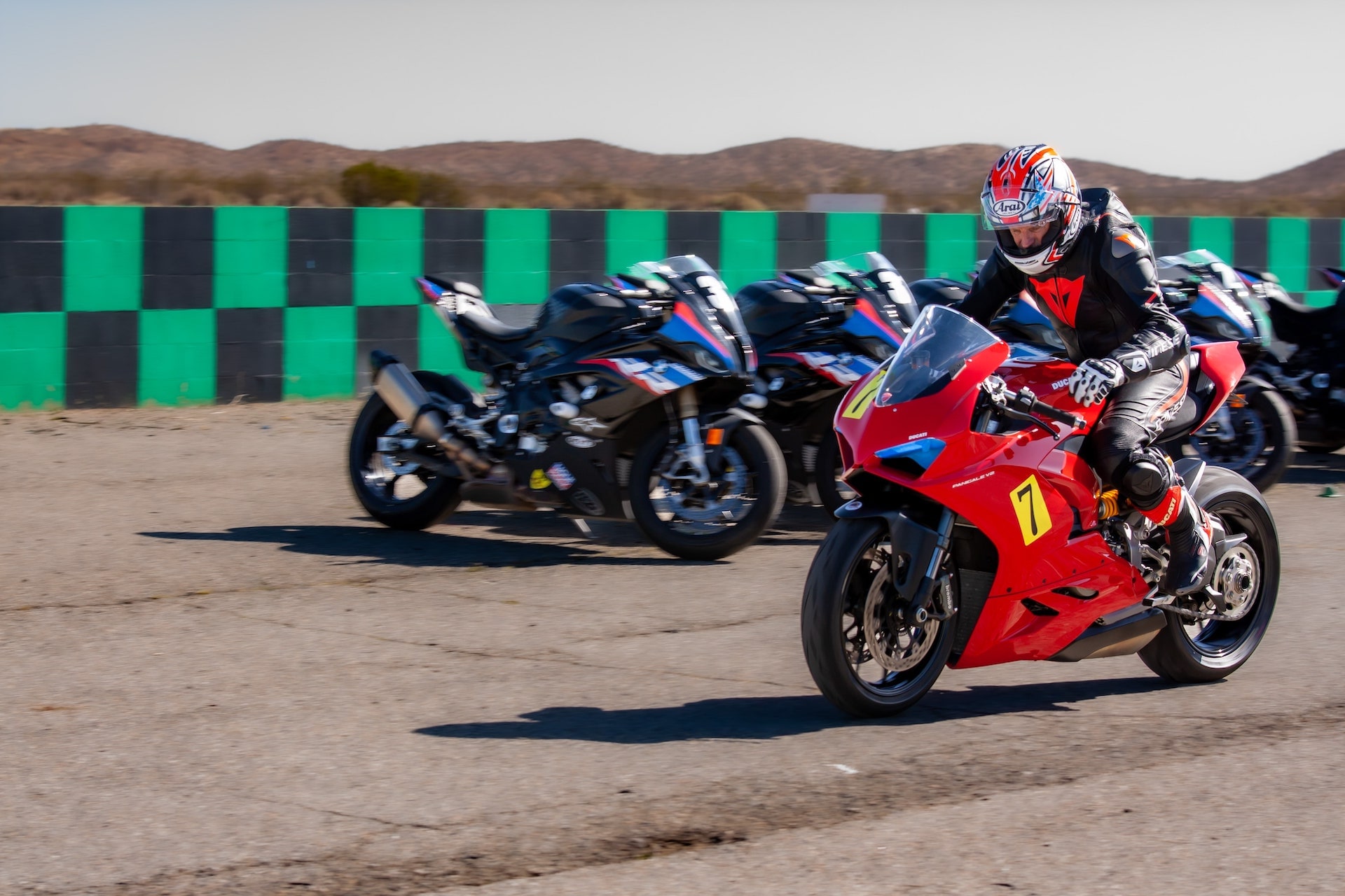 DROC track days at Streets of Willow 8 A rider on a red Ducati Panigale number 7 waits on the tarmac in front of a line of bikes and the green and black checkered wall at Streets of Willow, April 2022