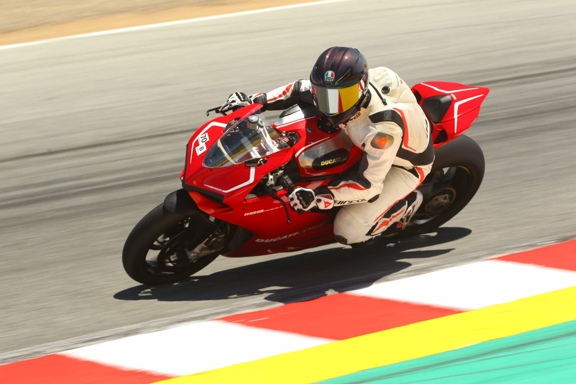 A rider in white leathers leans a red Ducati 1199 Panigale around a corner at Laguna Seca, July 2022