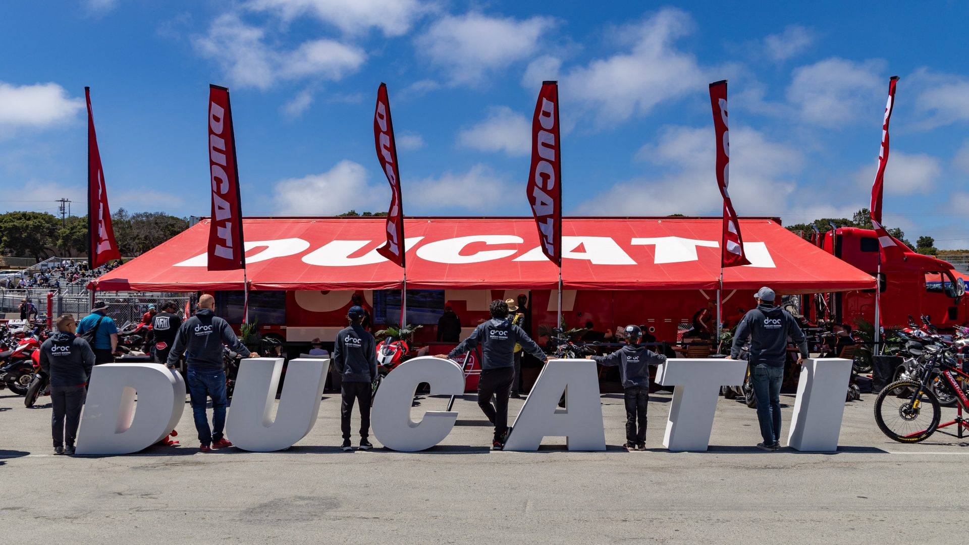 Ducati enthusiasts at a motorcycle event with large Ducati letters and flags in Orange County