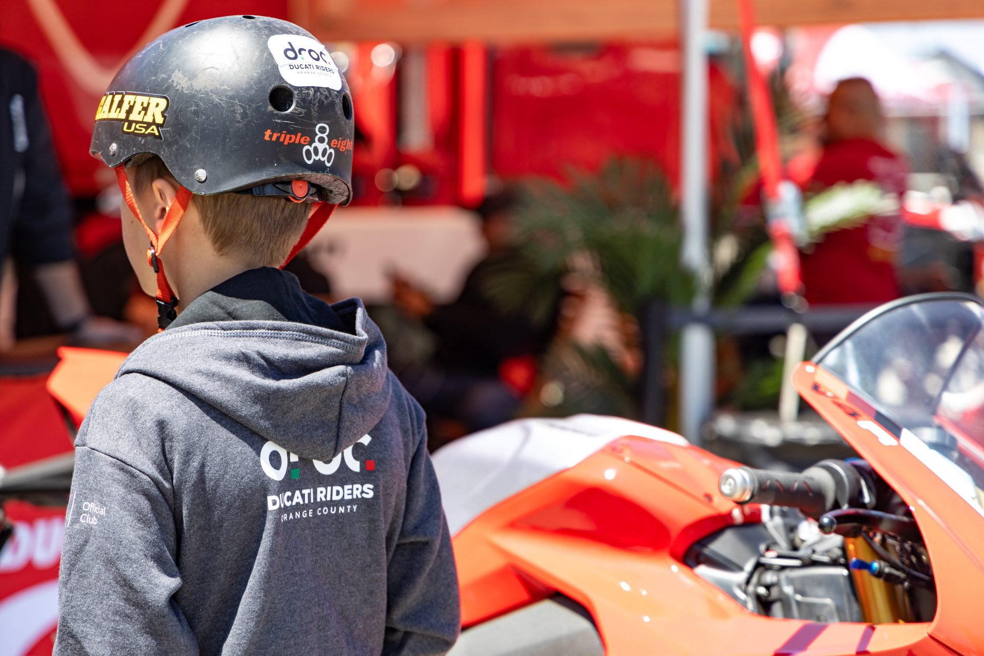 Young rider in Ducati Riders of Orange County hoodie admires a Ducati bike at an event