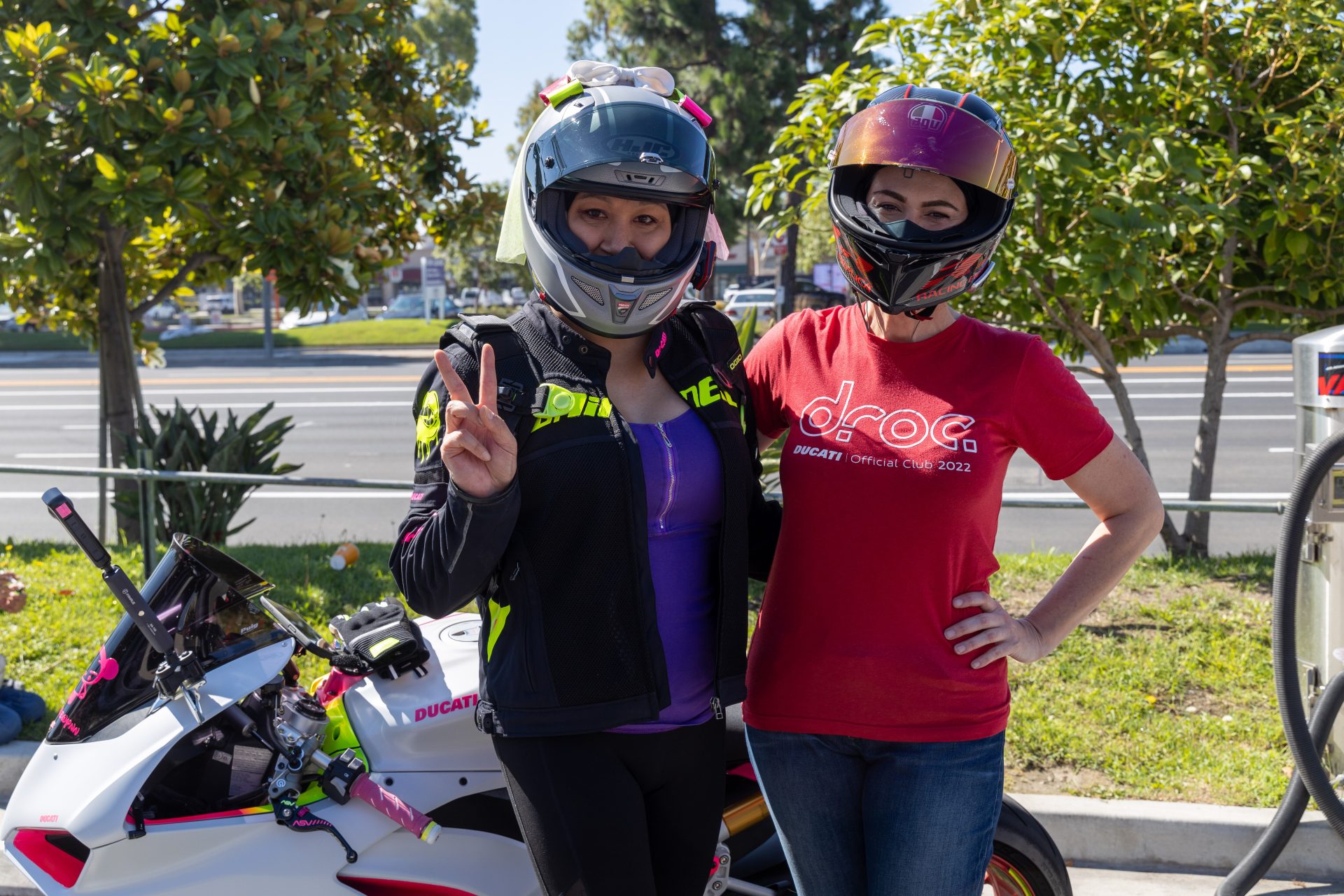 Two female riders in helmets and jackets pose together near a Ducati bike in Orange County