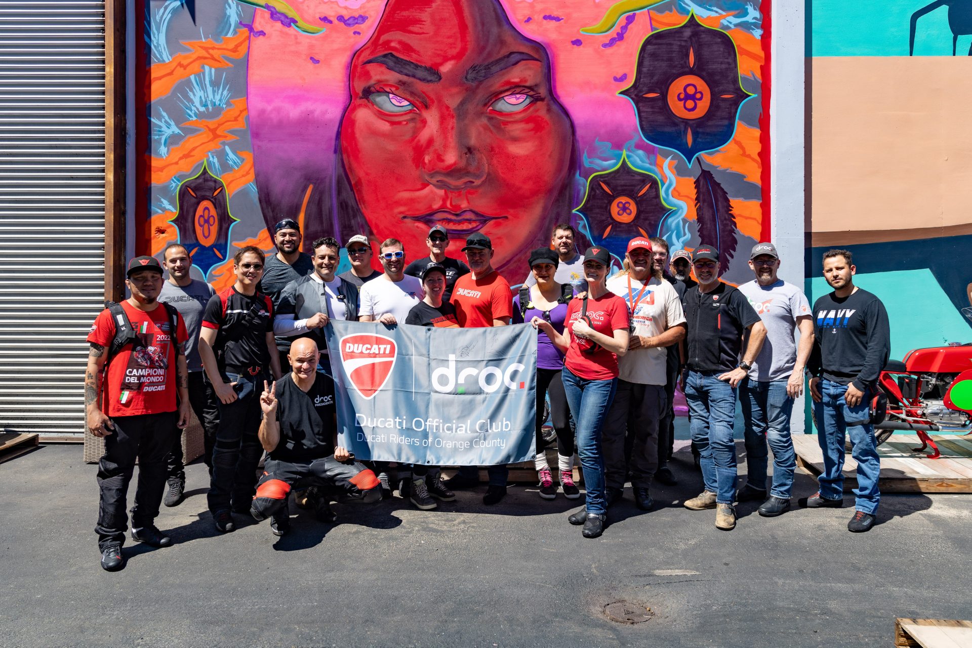 DROC members gather for a group photo in front of vibrant mural in Orange County, celebrating Ducati culture and camaraderie