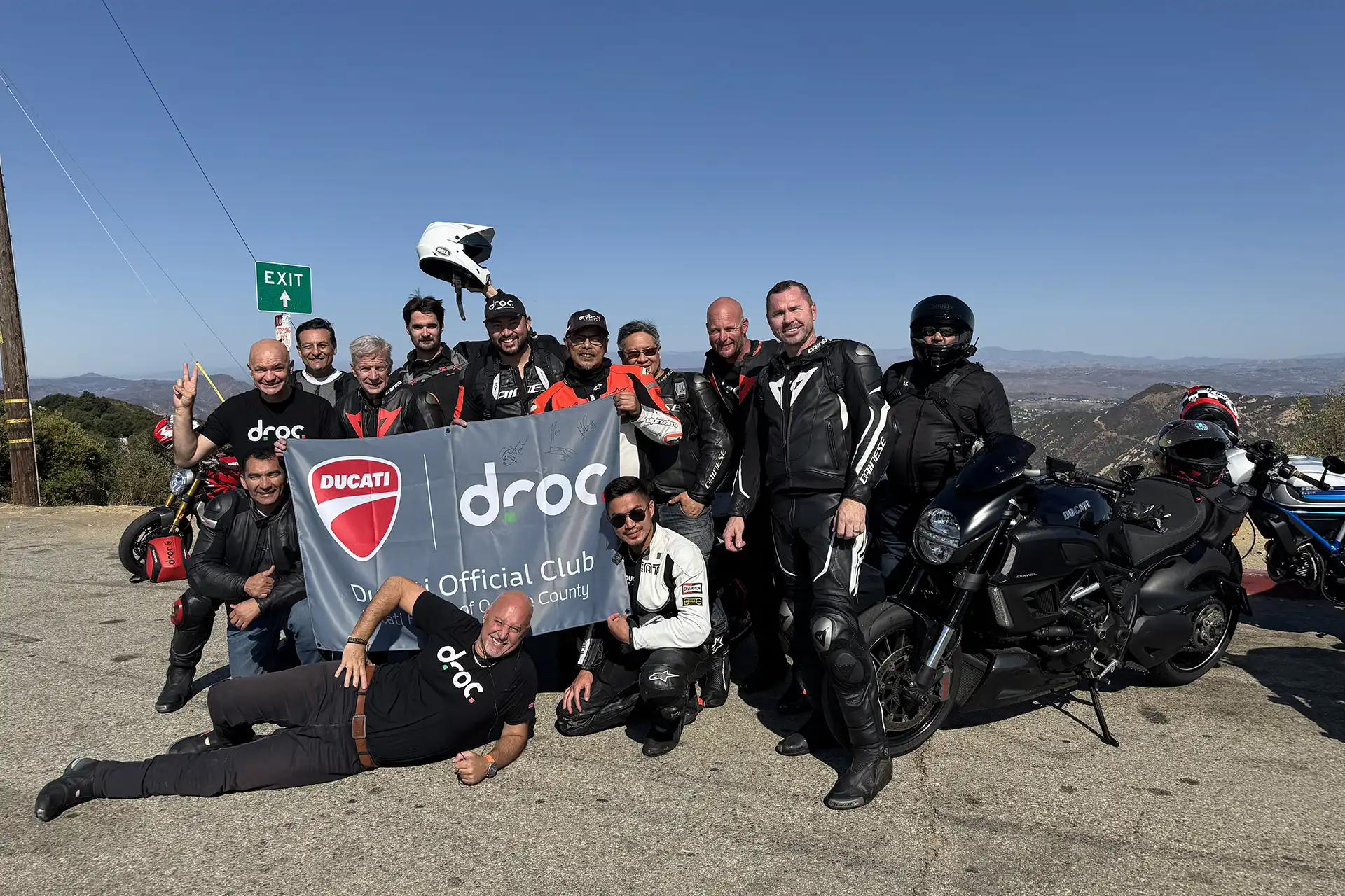 Ducati riders celebrating at Mulholland with DROC banner, showcasing the benefits of club membership in Orange County