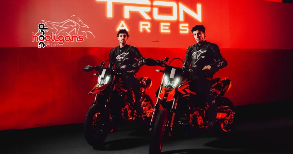 Two riders in black gear with motorcycles under red light in front of a glowing Tron Ares sign