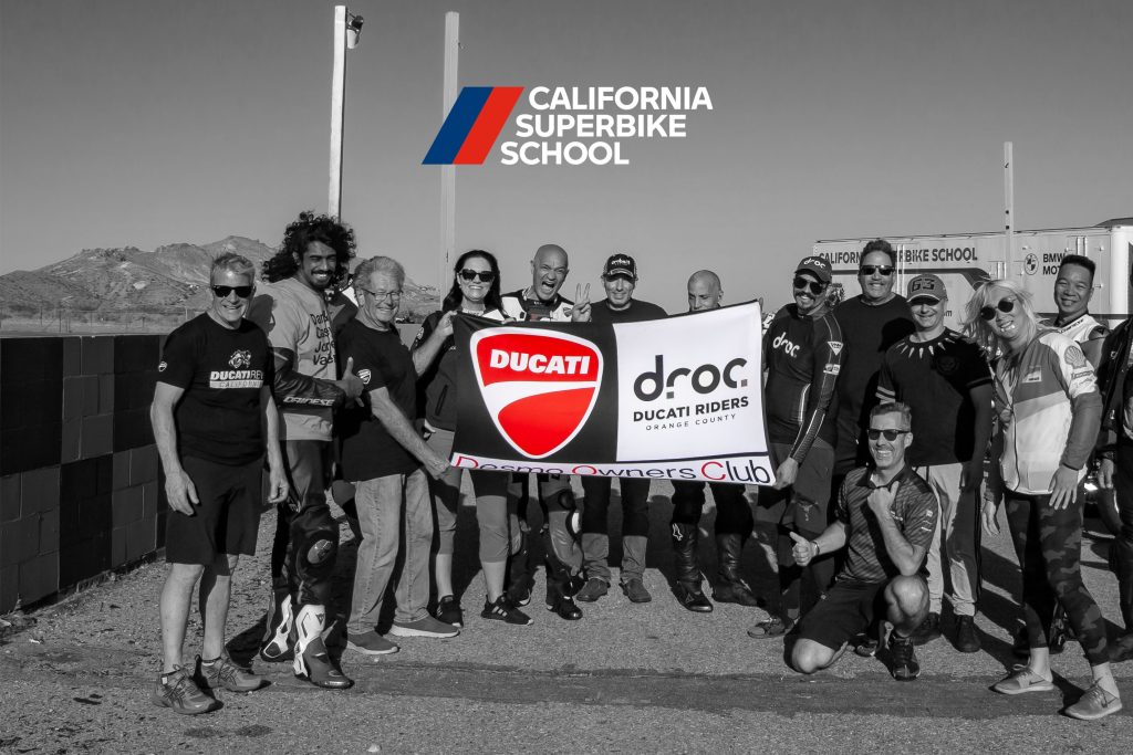 Ducati Riders of Orange County group at California Superbike School event with Ducati flag and mountain backdrop