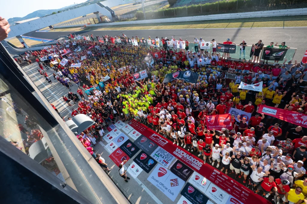 Ride with DROC: the six ways we ride 28 Hundreds of Ducati Official Club members gathered on the circuit at World Ducati Week 2026, behind rows of club banners