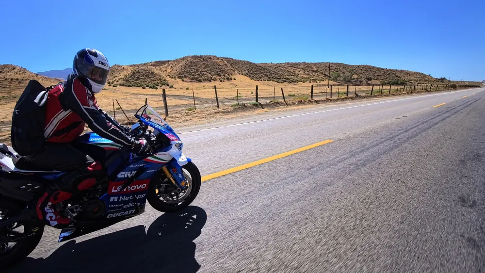 Motorcycle rider in a red and black suit on a sport bike with a Ducati logo on a road with a desert landscape.