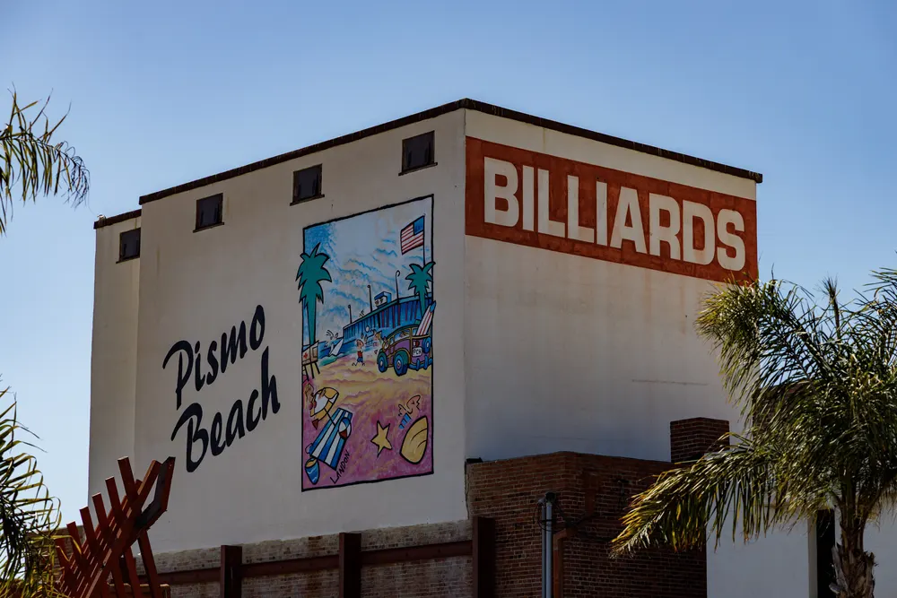 Pismo Beach mural on a building with the word "BILLIARDS" above it, featuring palm trees and a beach scene
