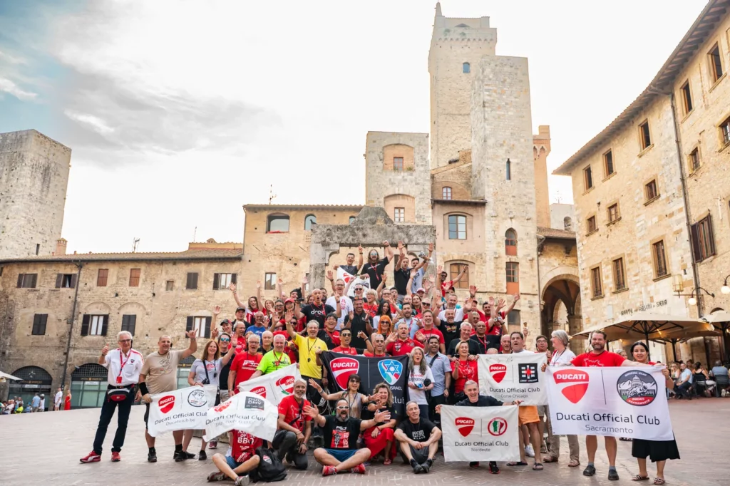 Ride with DROC: the six ways we ride 29 Ducati Official Club members holding their club banners in the piazza at San Gimignano, Tuscany