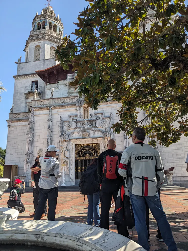 Group of people in motorcycle jackets standing in front of a large, ornate building with a tower and decorative entrance.