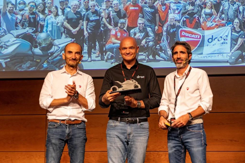 Ducati Riders of Orange County Named Ducati's Most Proactive Club Worldwide 1 Ducati club members celebrate at an event, with a motorcycle displayed in the background and DROC banner visible