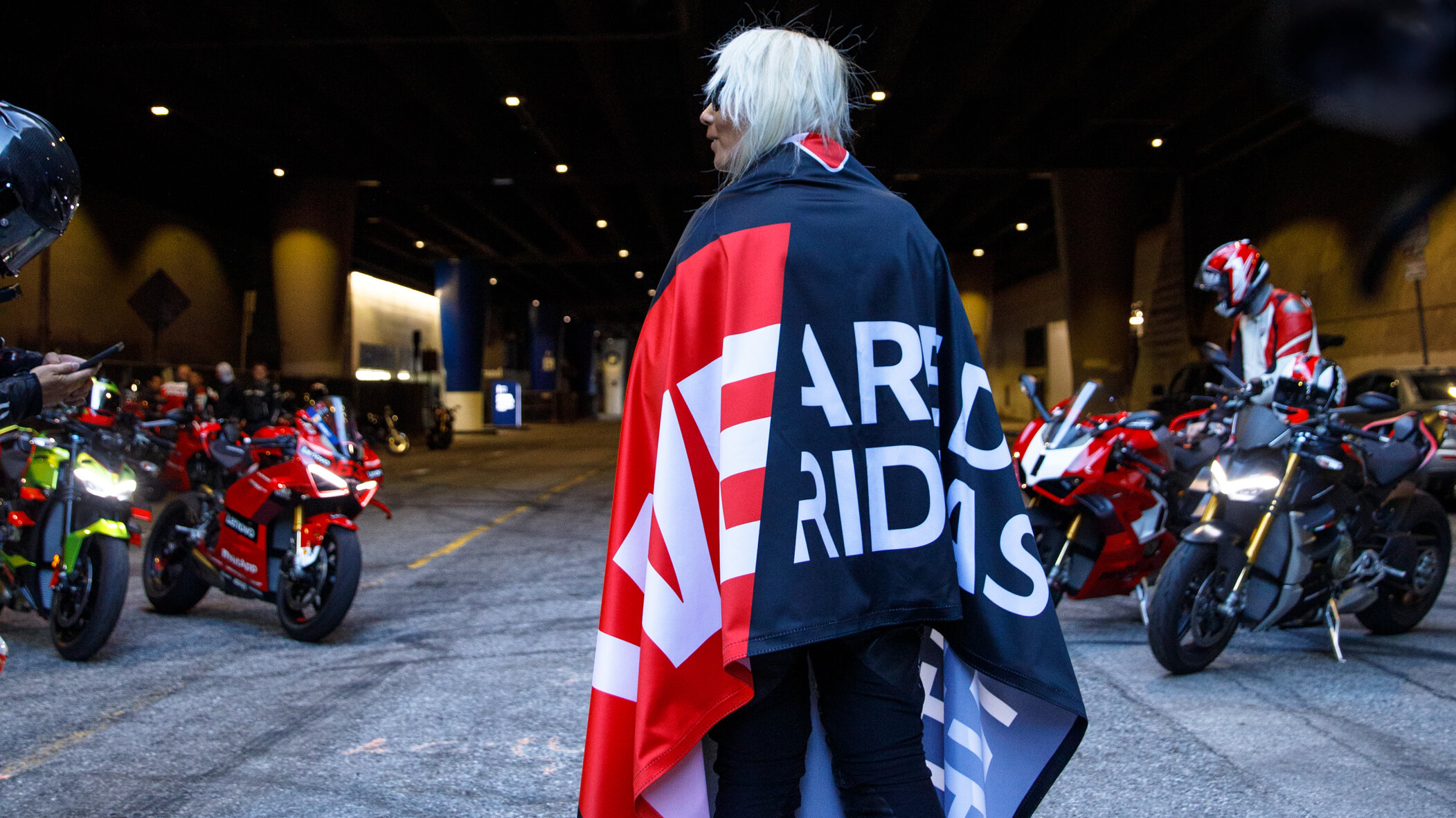 Member Stories 1 DROC member draped in the We Are Ducati We Ride As One flag in a Los Angeles tunnel, Ducatis lined up behind, 2024
