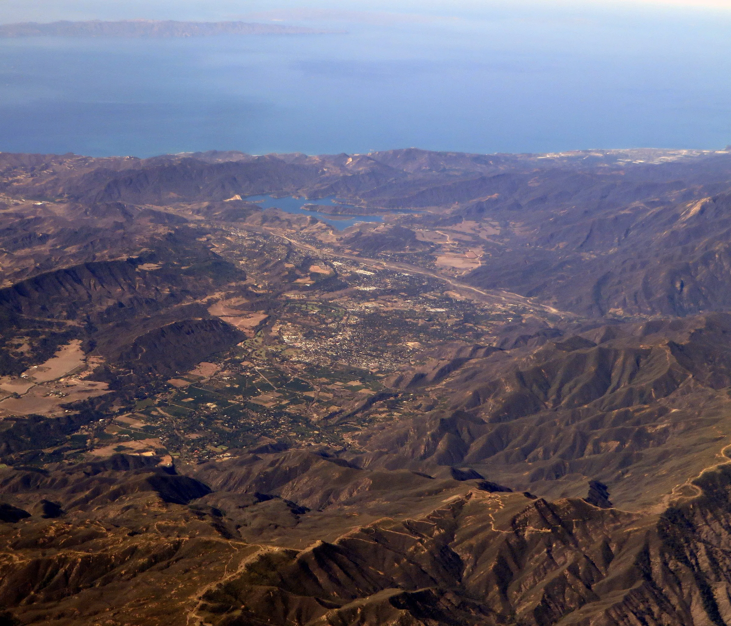 Aerial view along the Ojai Valley in Ventura County, the town spread between dry ridgelines with Lake Casitas and the Pacific coast beyond