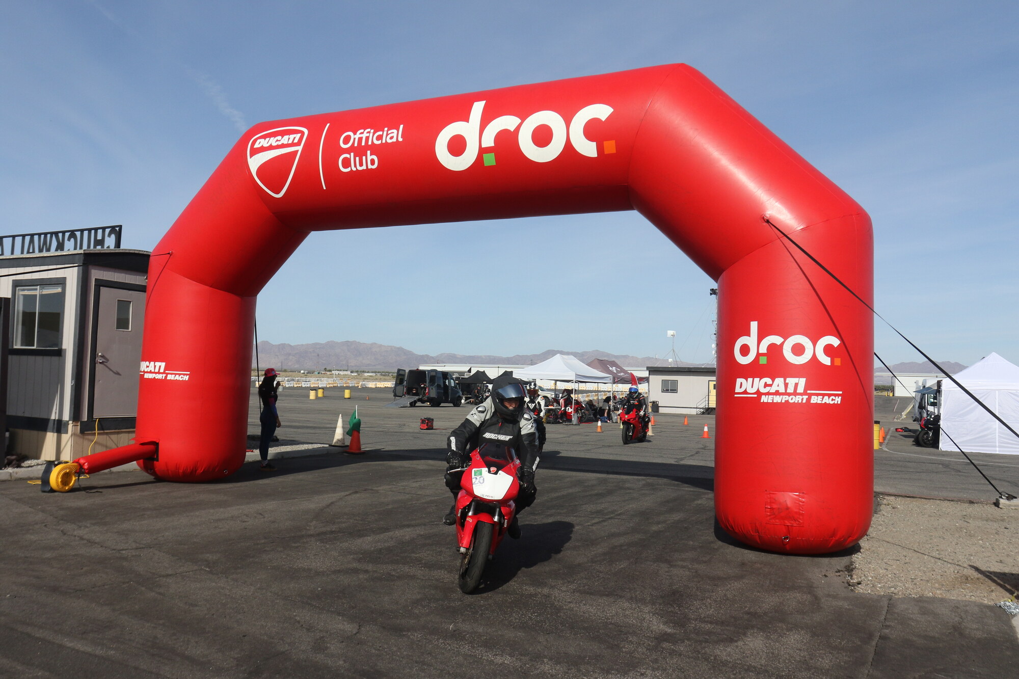 Patrick Pallan riding his red and white Ducati out under the red DROC arch at Chuckwalla Valley Raceway