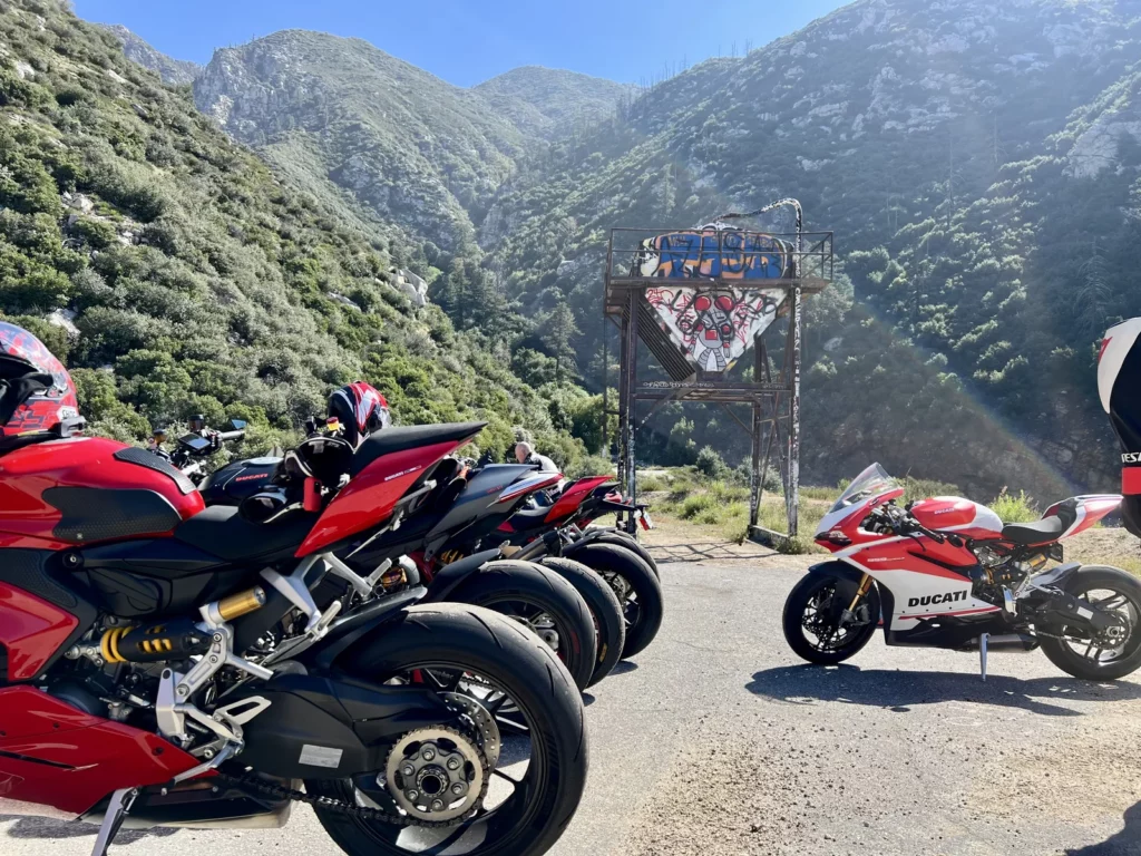 Azusa and Carbon Canyon rides 1 Line of sport bikes parked on pavement facing a metal graffiti-covered structure with mountains behind, Azusa