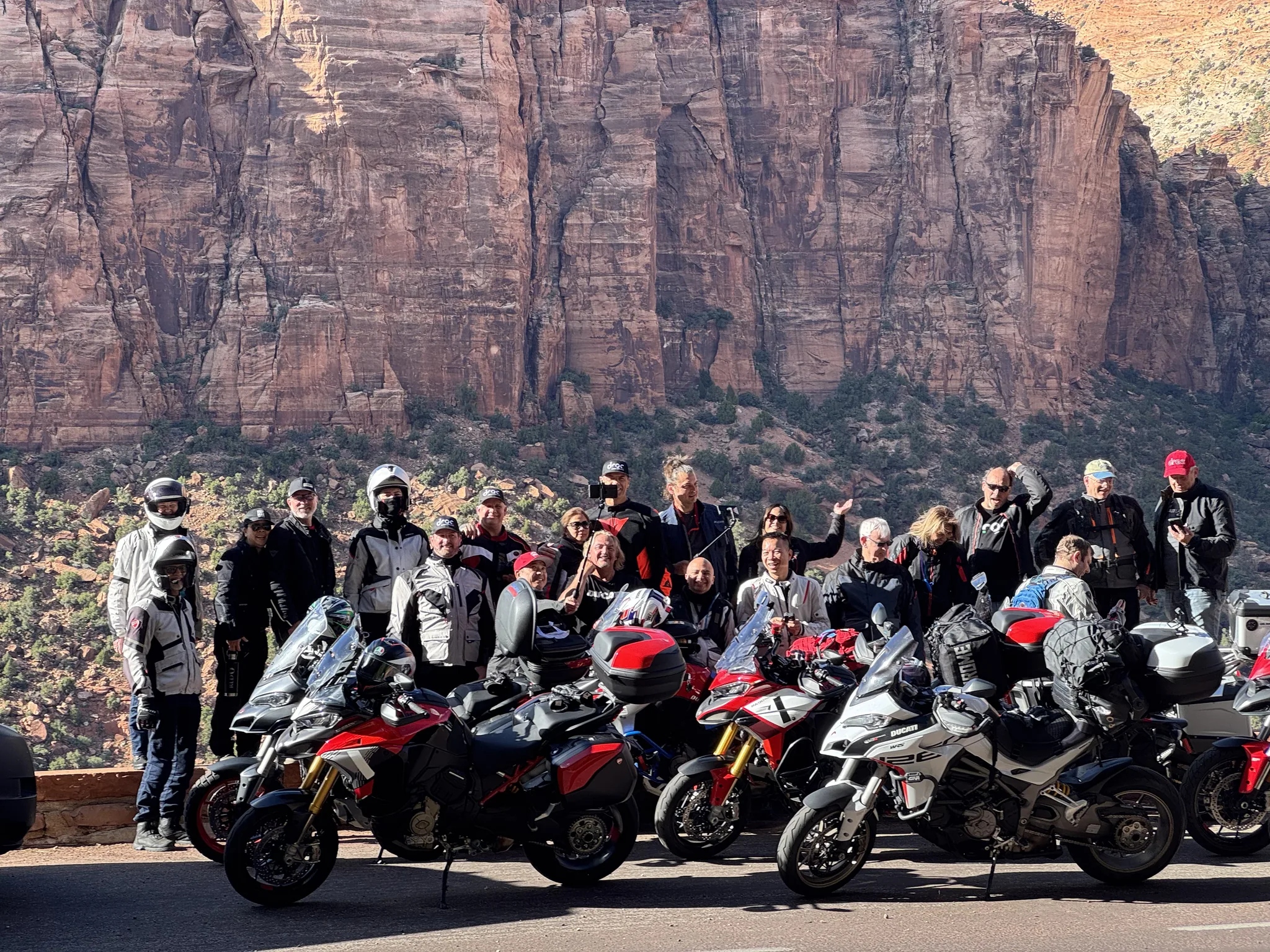 Around twenty DROC riders stand behind a row of parked Ducatis below the red sandstone walls of Zion Canyon.