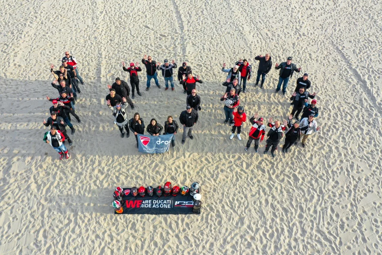 Aerial view of DROC riders and Ducatis formed into the number 100 on the sand, We Ride As One 2026