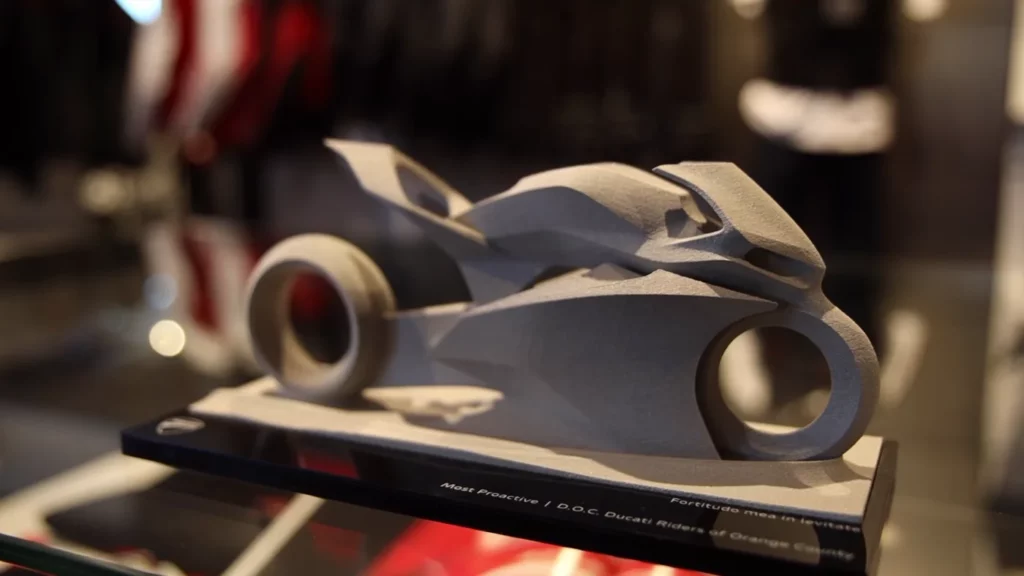 Abstract 3D-printed motorcycle sculpture on a display base labeled "Most Proactive | D.O.C. Ducati Riders of Orange County