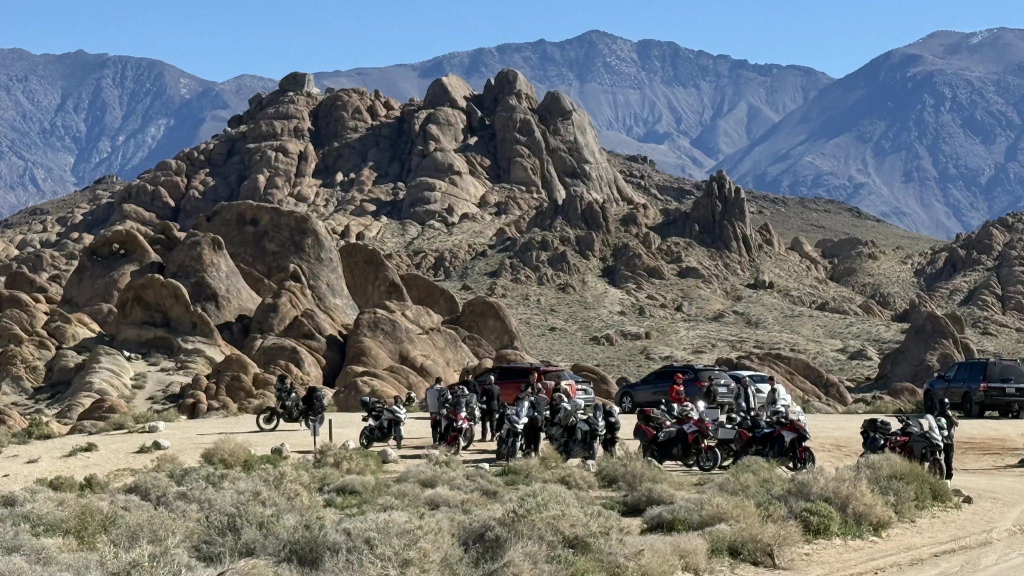 Weathered granite formations in the Alabama Hills, with a group of loaded adventure bikes parked on the flat below and the Sierra Nevada behind.