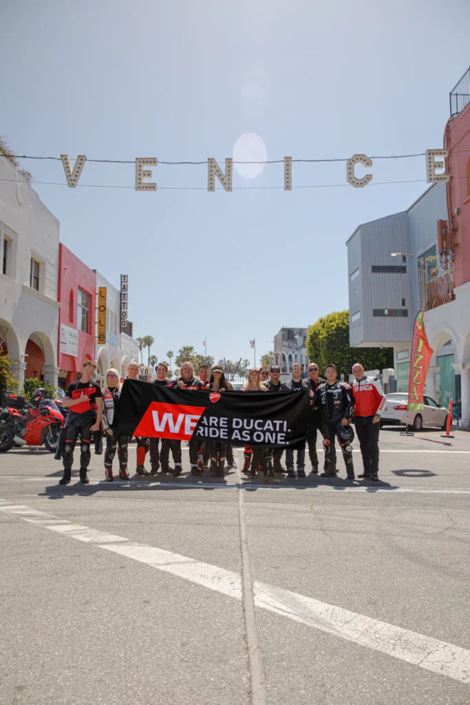 Ducati riders gather in Venice, holding a banner that reads "WE ARE DUCATI. RIDE AS ONE."