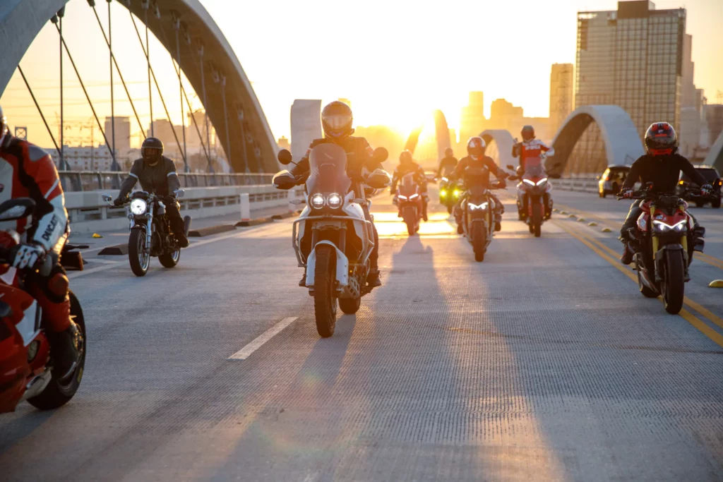 Ride with DROC: the six ways we ride 6 Riders crossing an arched city bridge into the sunset, downtown skyline behind them