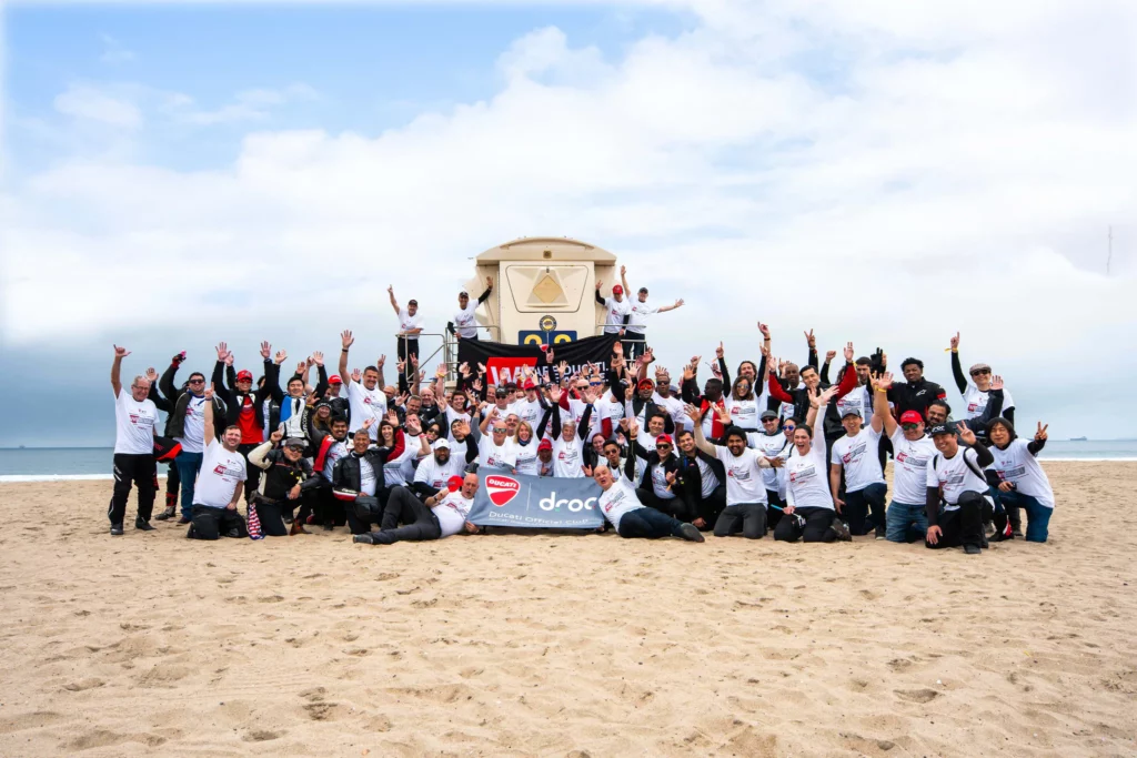 Ride with DROC: the six ways we ride 23 Large group on the sand around a lifeguard tower, holding a DROC Ducati Official Club banner