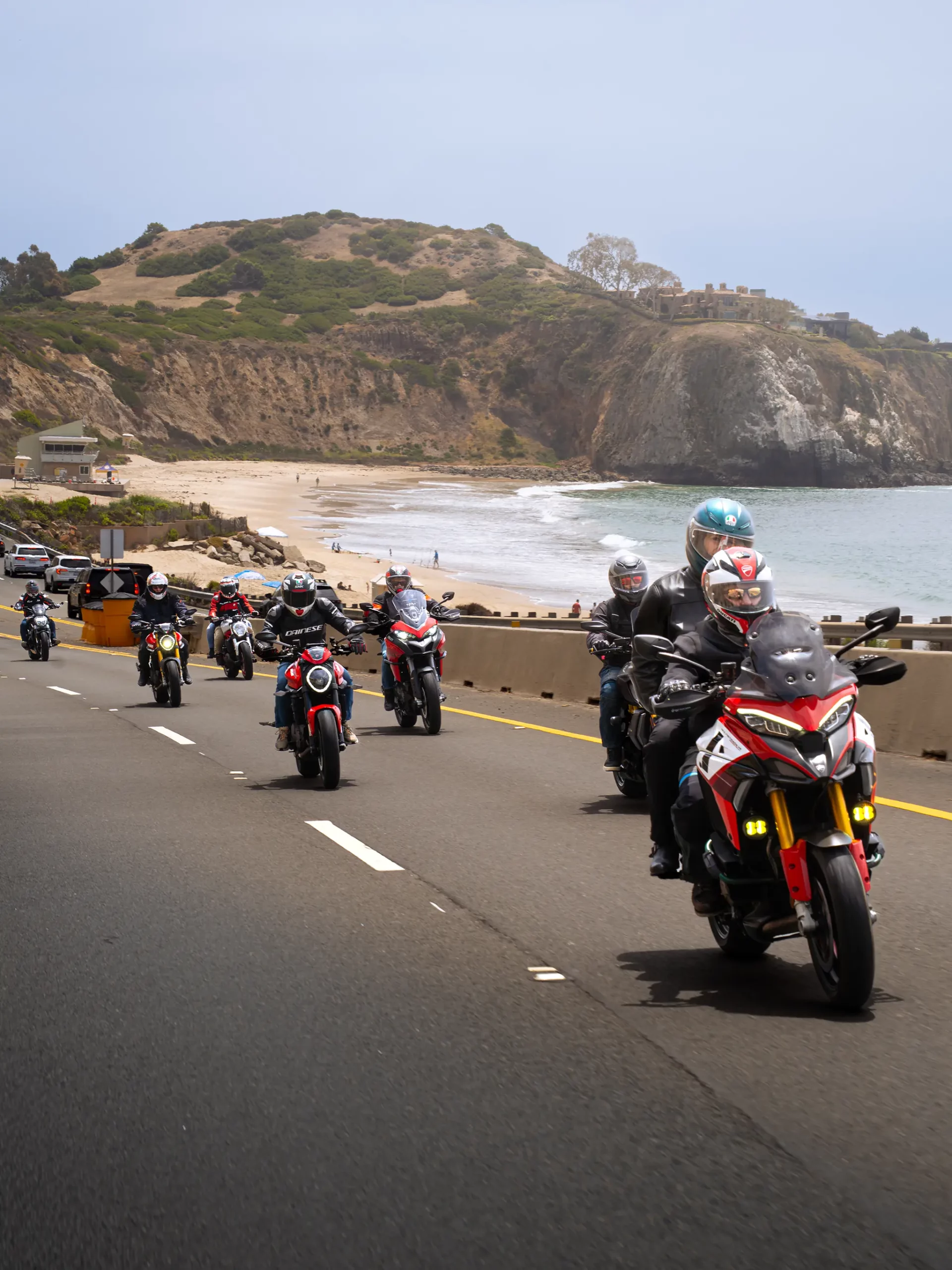 We Ride As One 1 Ducati motorcycles riding along the coast with a beach view, enjoying scenic group rides by the ocean