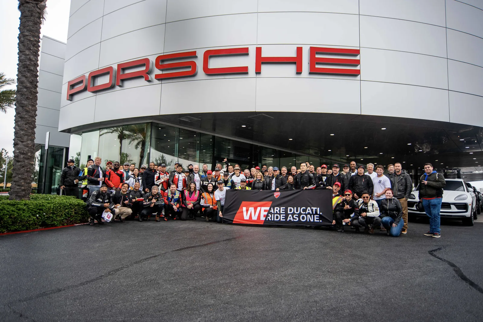 Ducati riders gather under the Porsche sign at Porsche Irvine with a We Are Ducati, Ride As One banner, May 3, 2025