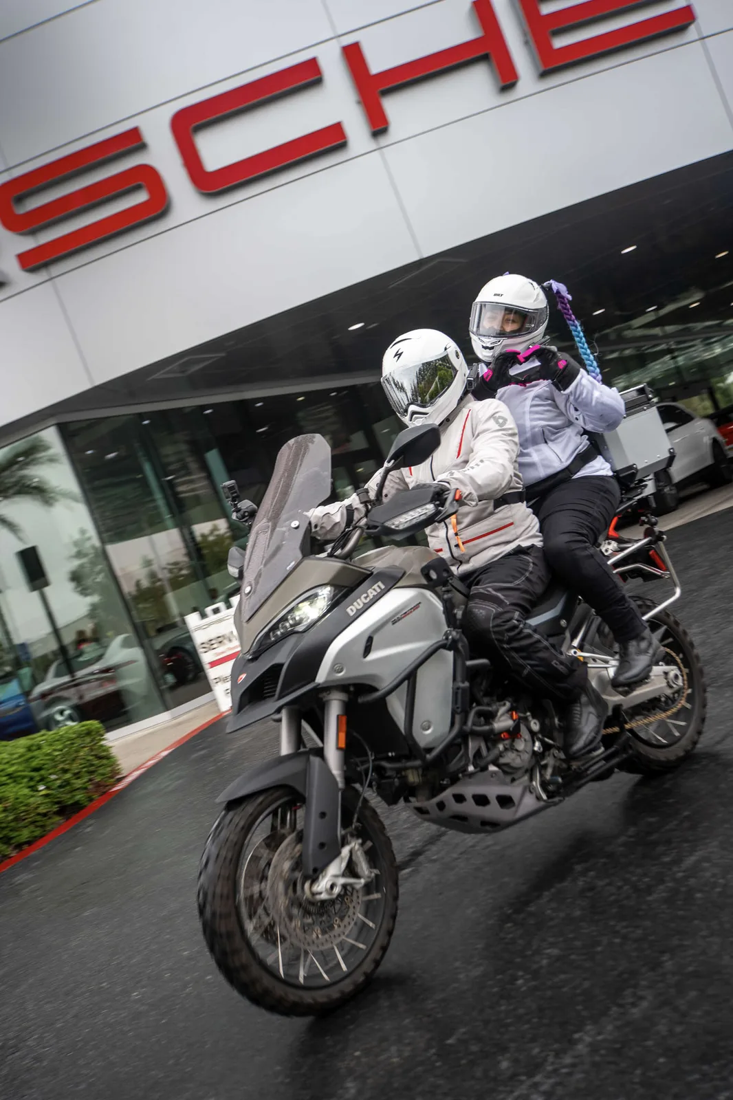 A rider and passenger on a Multistrada Enduro roll past the Porsche sign at Porsche Irvine, We Ride As One 2025