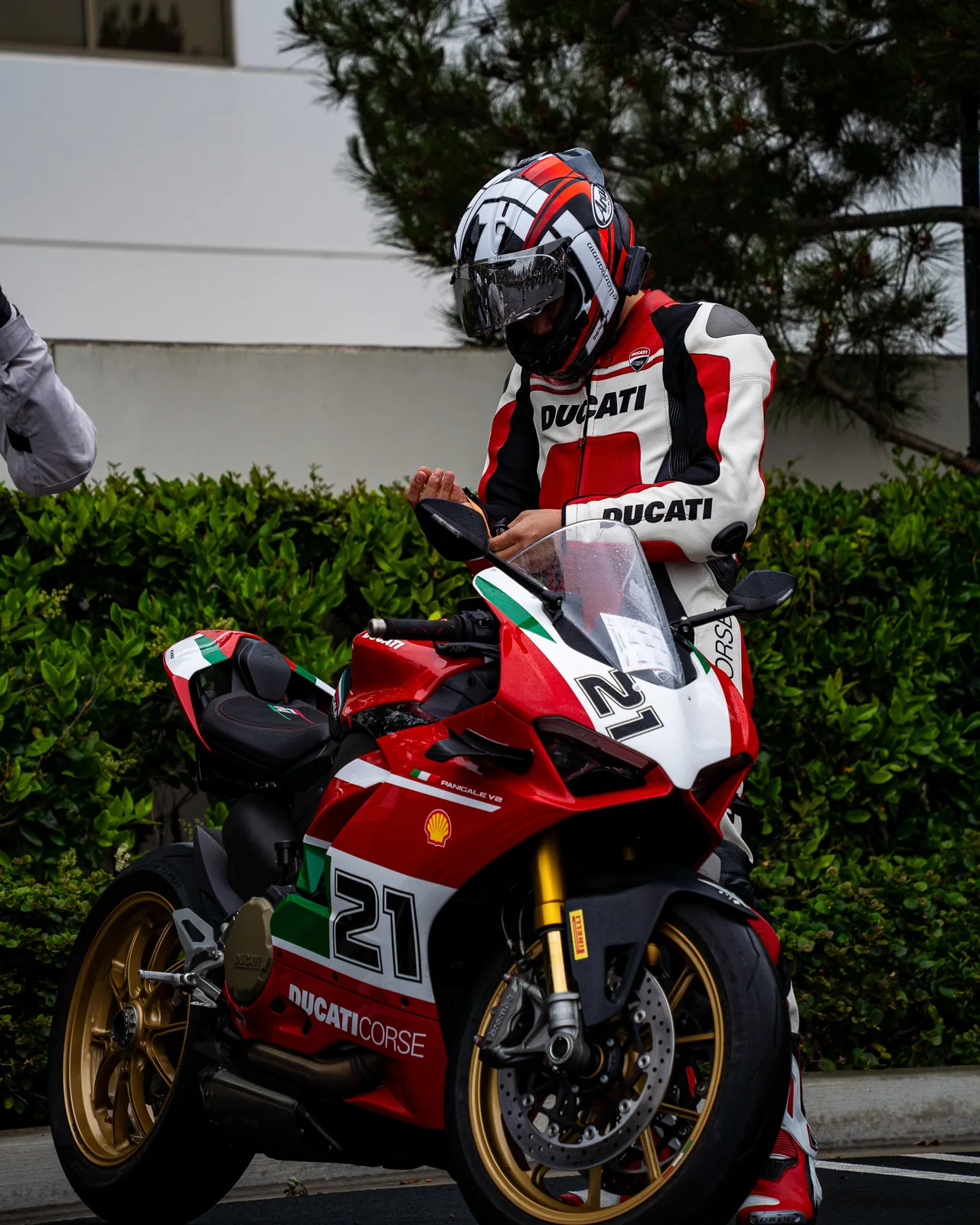 A rider in Ducati leathers gears up beside a Panigale V2 in number 21 Troy Bayliss livery at Porsche Irvine, May 2025