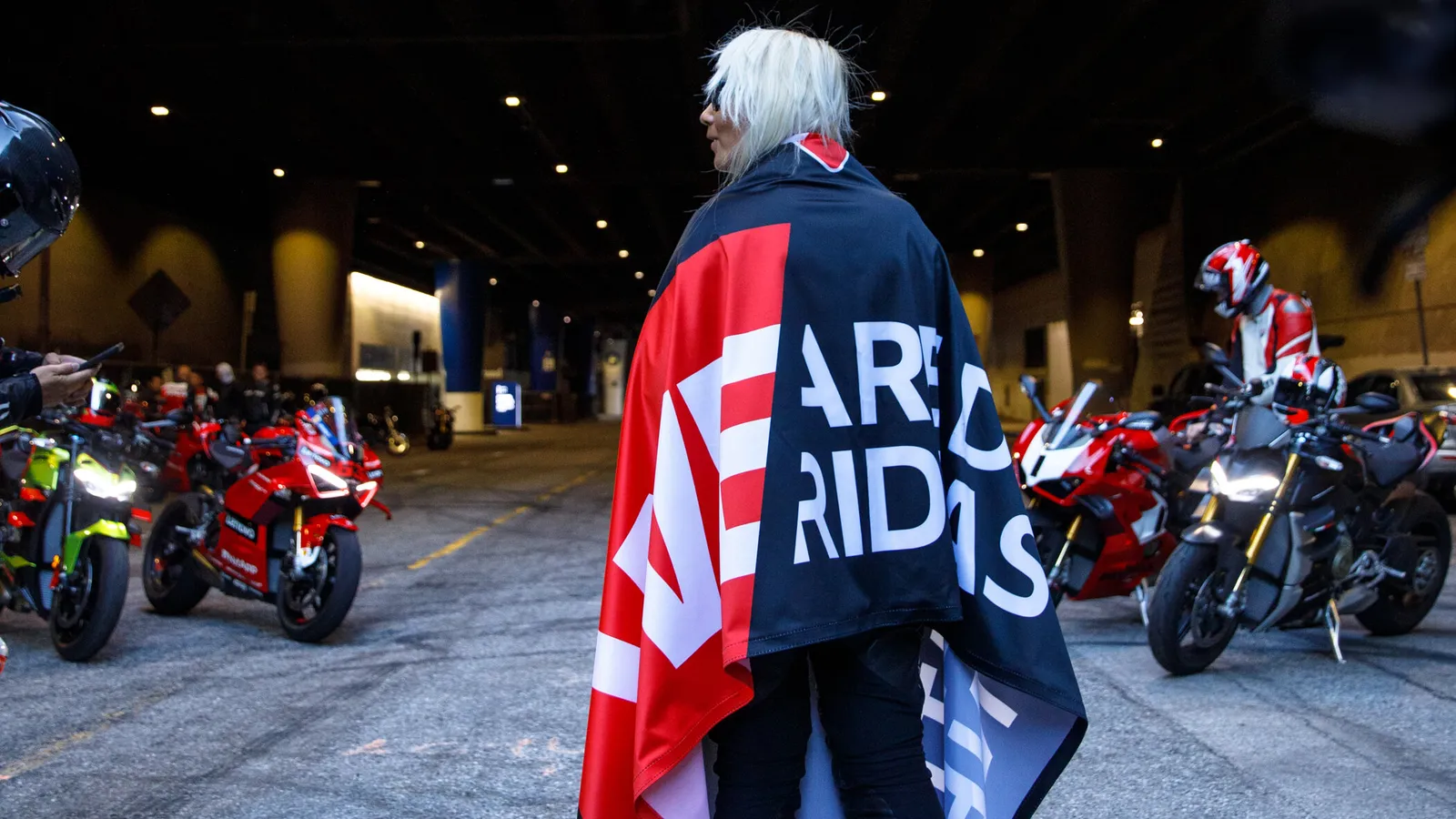 DROC member draped in the We Are Ducati We Ride As One flag in a Los Angeles tunnel, Ducatis lined up behind, 2024