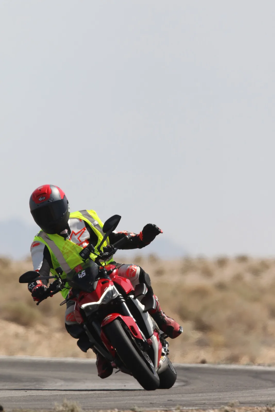 A rider in a fluorescent vest on a red Ducati with the number 45 leans through a corner at Chuckwalla Valley Raceway, desert scrub behind, March 2026