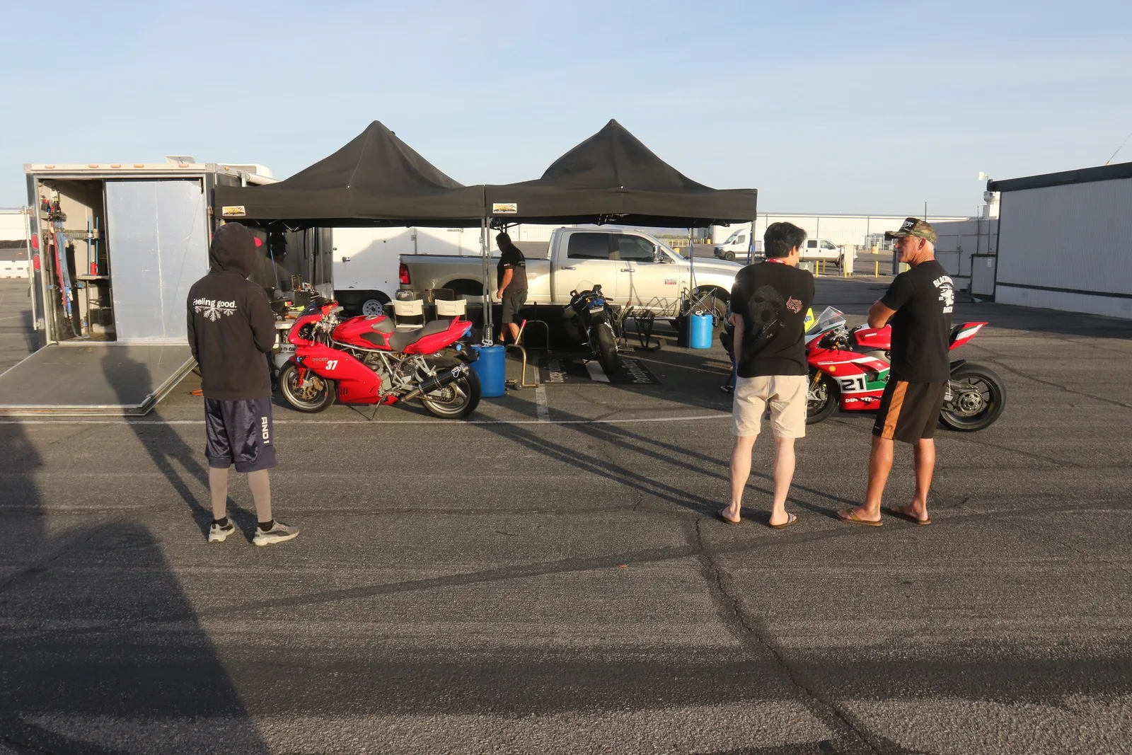 Two red Ducatis parked beside a trailer under black pop-up tents in the Chuckwalla Valley Raceway paddock in the early morning, March 2026
