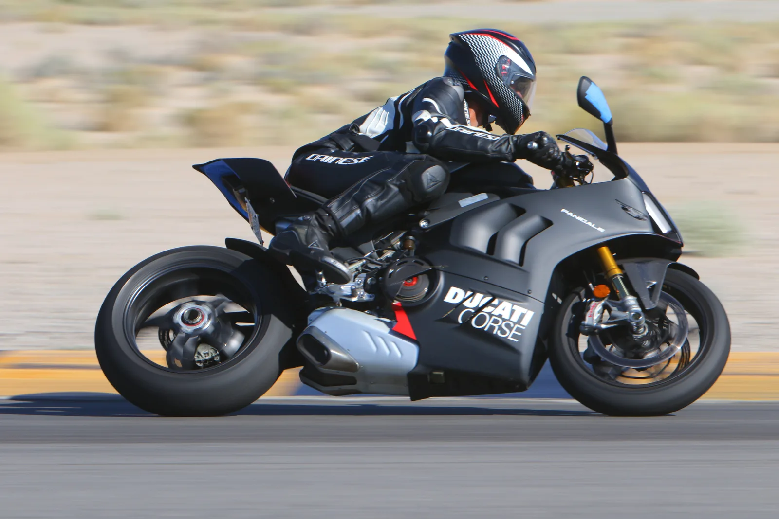 A rider leaned over on a black Ducati Panigale V4 with Ducati Corse livery, desert blurred behind, Chuckwalla Valley Raceway, September 2023