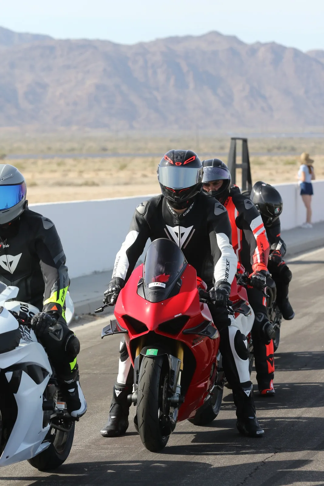 Four helmeted riders line up on their motorcycles beside a white wall, a red Ducati Panigale V4 in front, with desert mountains behind at Chuckwalla Valley Raceway, March 2026