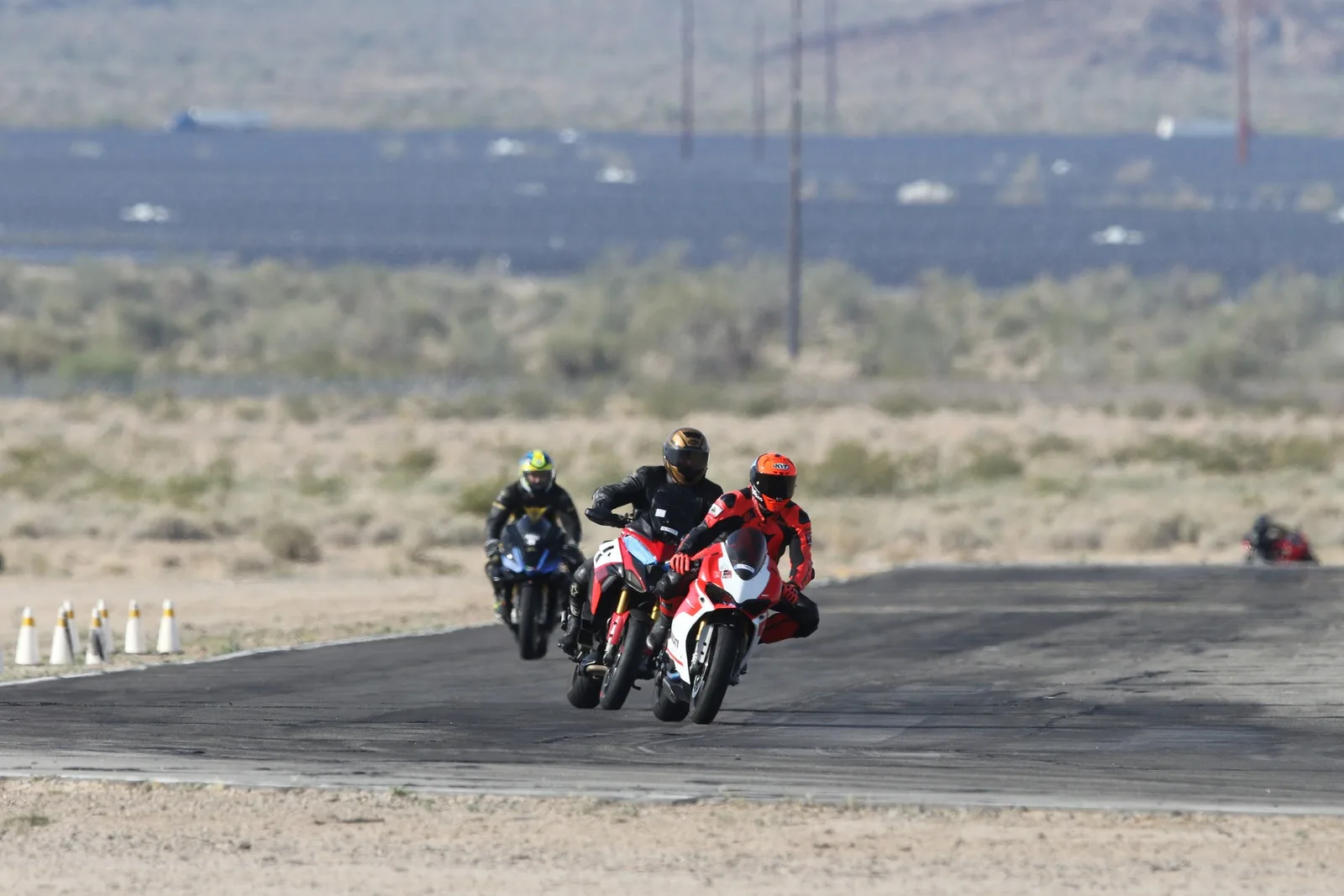Three riders in a line on motorcycles, a red and white Ducati Panigale leading, exit a corner at Chuckwalla Valley Raceway with open desert behind, March 2026