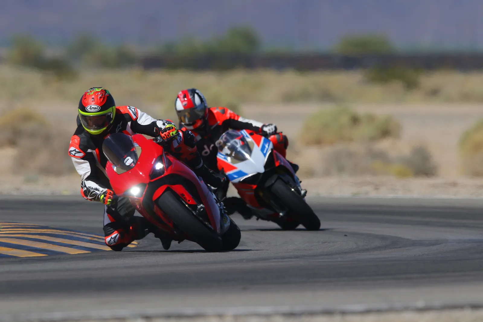 Two Ducati Panigales lean into a corner over the yellow and black curbing at Chuckwalla Valley Raceway, September 2023