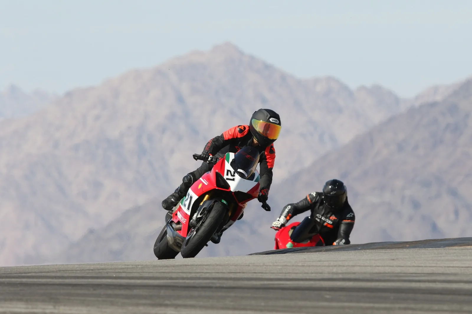 A Ducati Panigale number 21 leans through a turn with a second rider behind it and desert mountains filling the background, Chuckwalla Valley Raceway, March 2026