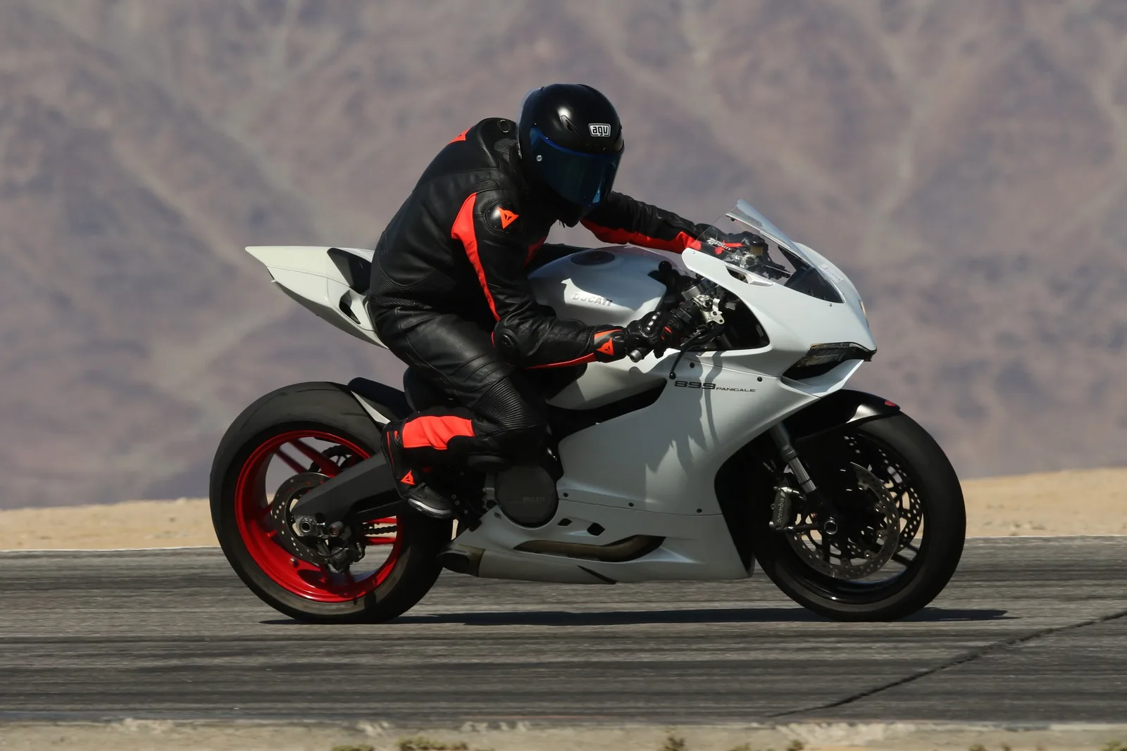 A rider in black and red leathers on a white Ducati 899 Panigale with red wheels on the track at Chuckwalla Valley Raceway, desert mountains behind, March 2026