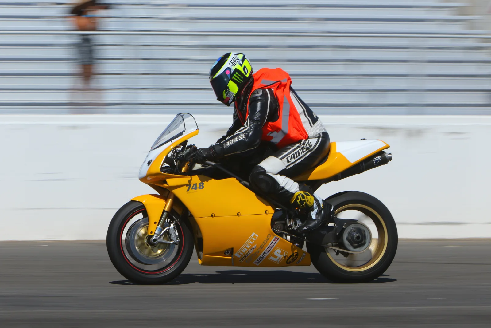 A rider in an orange vest on a yellow Ducati 748 passes the pit wall at Chuckwalla Valley Raceway, September 2023