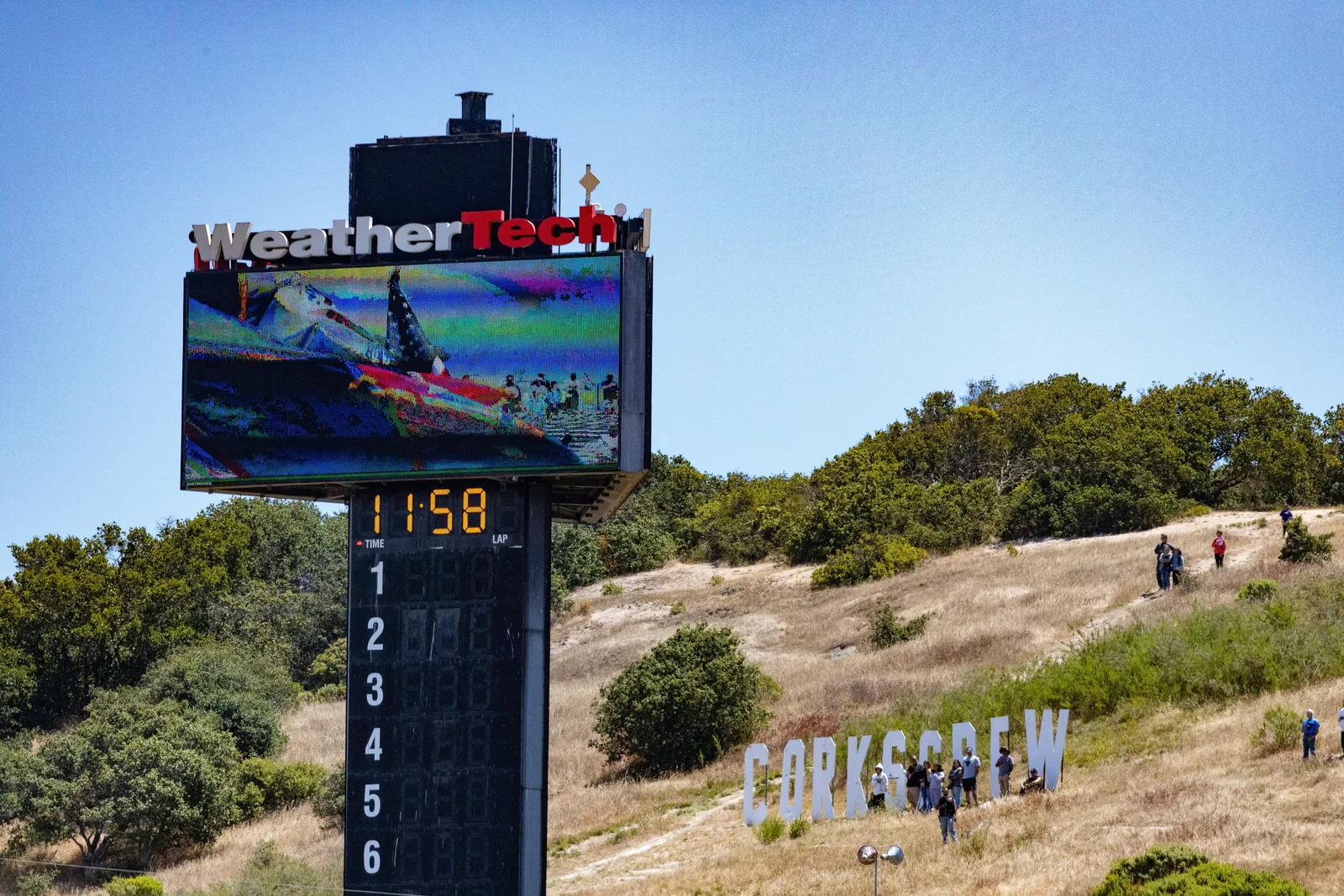 The Corkscrew sign on the hillside above WeatherTech Raceway Laguna Seca beside the timing tower, with spectators on the slope, MotoAmerica weekend, July 2023