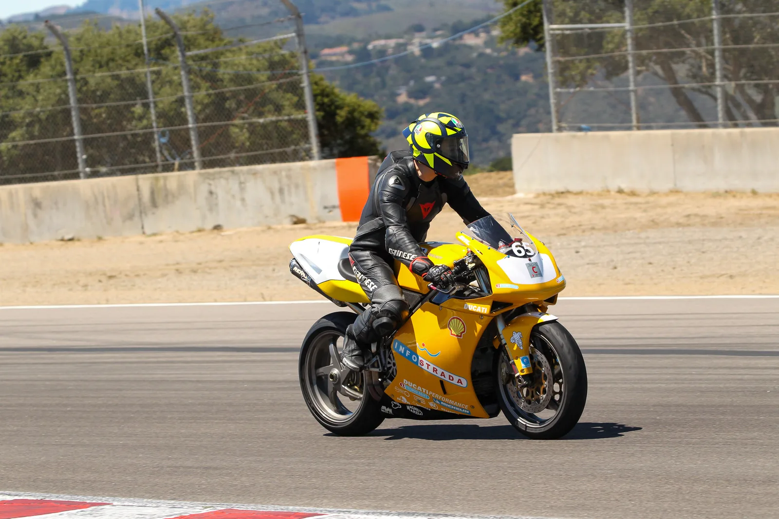 A rider in black leathers on a yellow number 65 Ducati in Infostrada livery rolls around Laguna Seca at the Ducati track day, July 2025