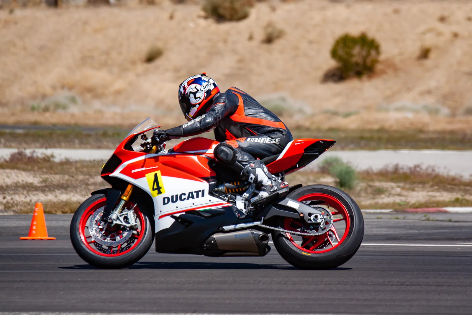 DROC track days at Streets of Willow 9 A rider in black and orange Dainese leathers leans a red and white Ducati Panigale number 4 through a turn at Streets of Willow, orange cone on the left, April 2022