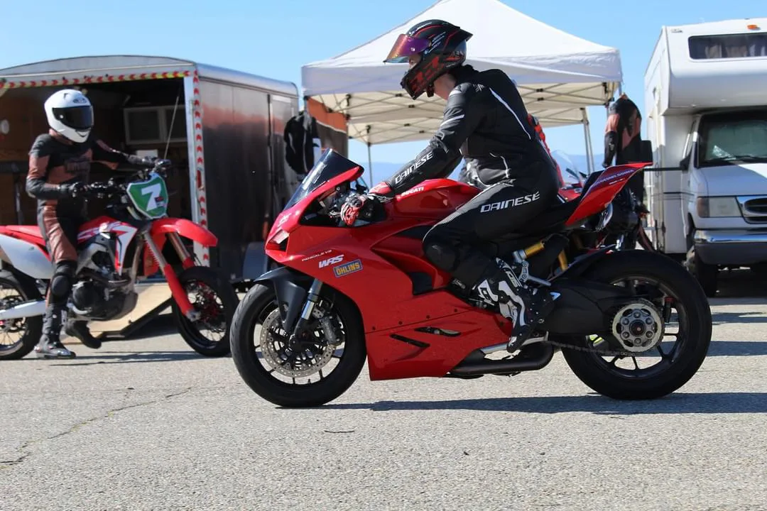 DROC track days at Streets of Willow 6 A rider in black Dainese leathers sits on a red Ducati Panigale V2 in the paddock at Streets of Willow, with a dirt bike and a white canopy behind, April 2024