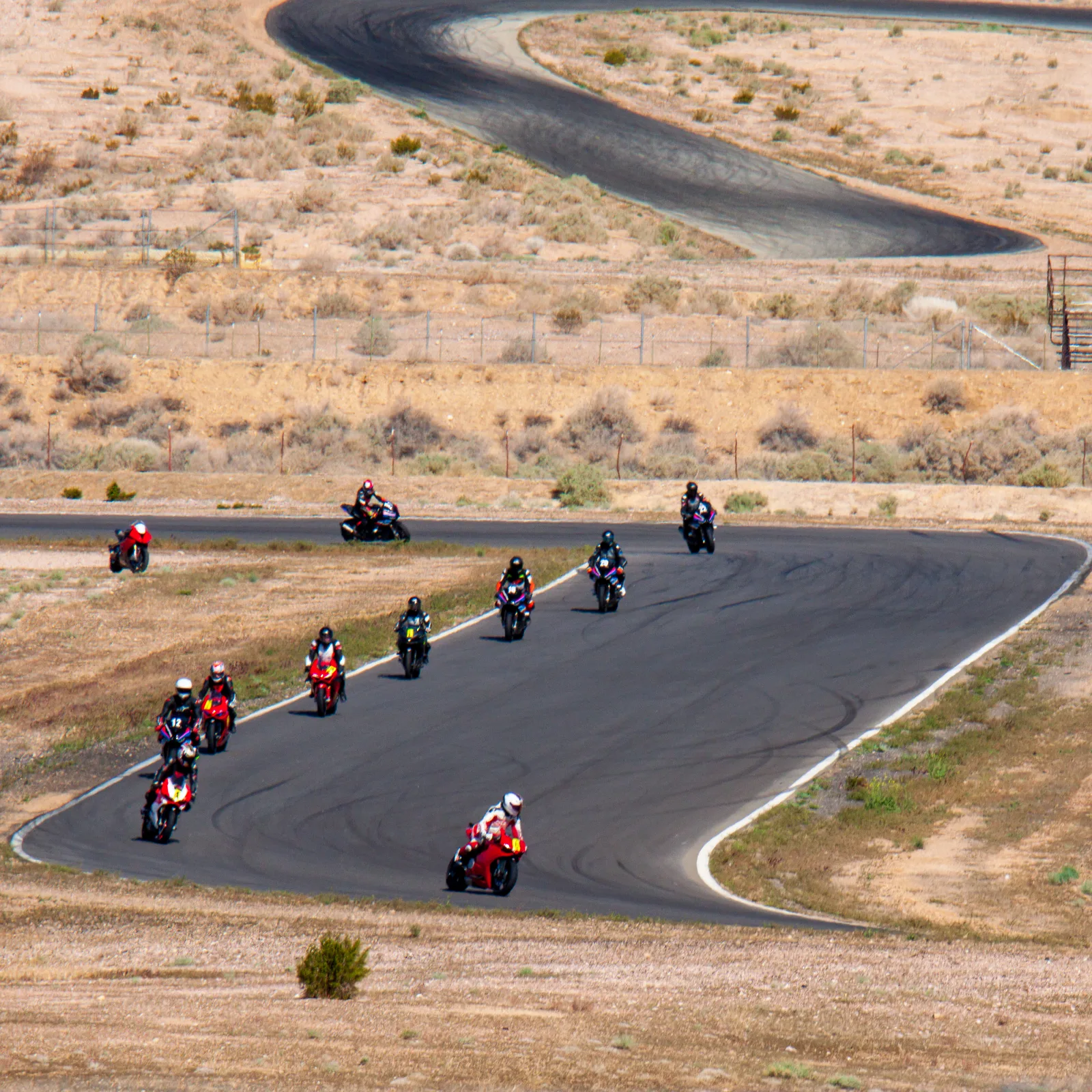 DROC track days at Streets of Willow 10 A group of riders, several on red Ducatis, follow each other through a wide corner at Streets of Willow with a looping section of track above them in the desert, April 2022