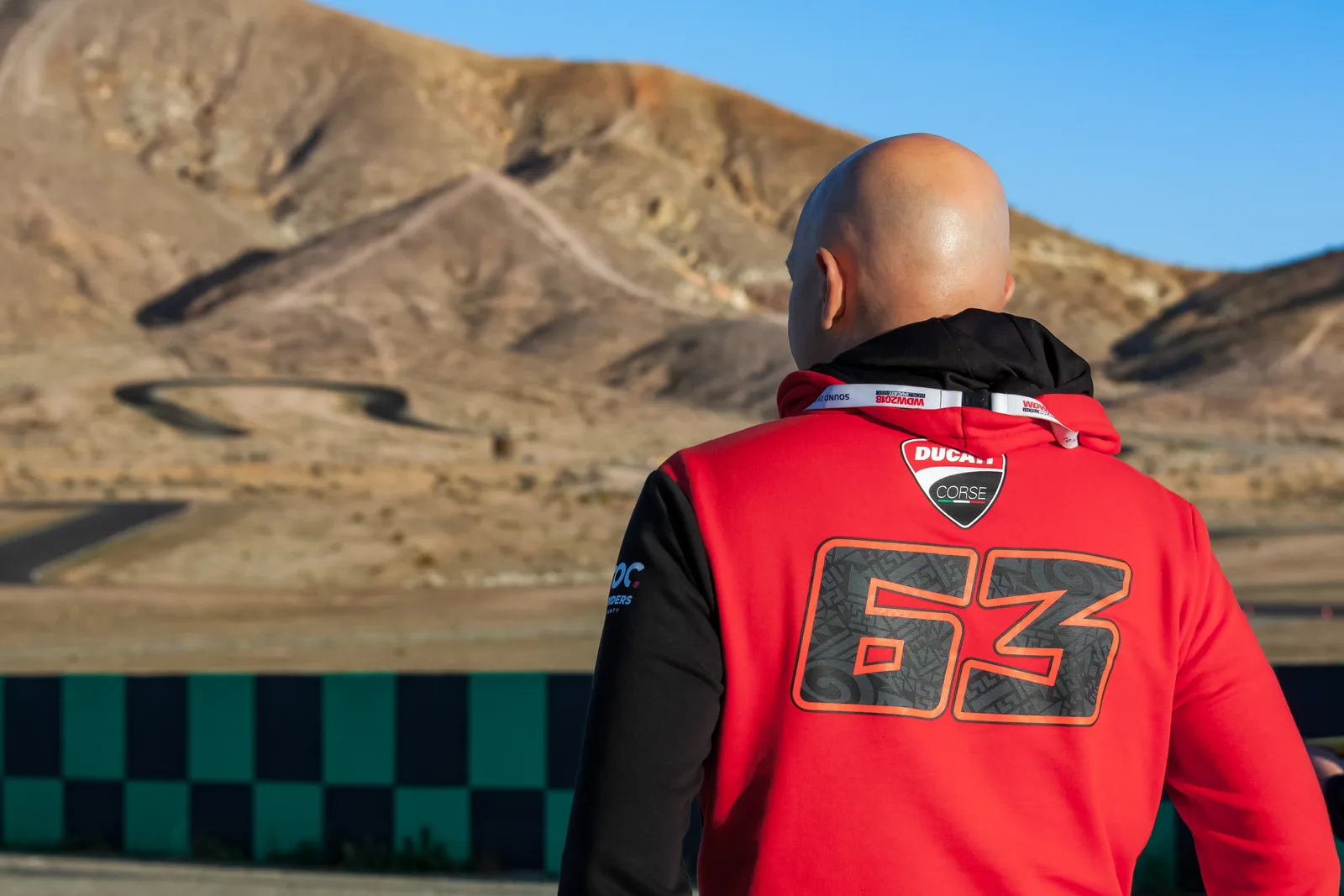DROC track days at Streets of Willow 4 A rider in a red Ducati Corse number 63 hoodie, seen from behind, looks across the Streets of Willow circuit toward the desert hills and a looping section of track, April 2022